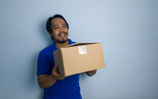 穿着蓝色t恤的东南亚微笑男子拿起一个盒子图片下载