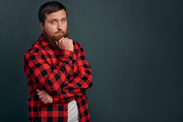 图片英俊的年轻胡子男子站在gey墙背景孤立。看相机。图片下载