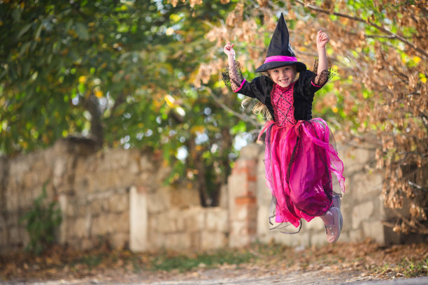 一个穿着女巫服装的小女孩在街上蹦蹦跳跳。万圣节的节日。本空间图片下载