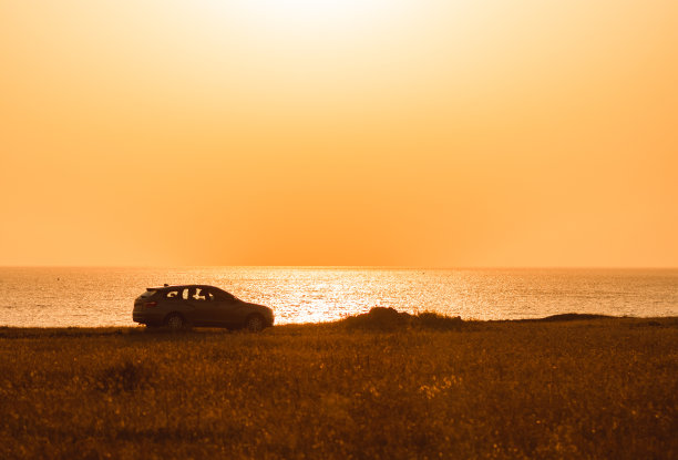 日落时海边悬崖上一辆汽车的剪影图片下载