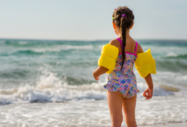 一个5岁的女孩穿着一件颜色漂亮的褶边泳装，站在海滩上想要下水去。图片下载
