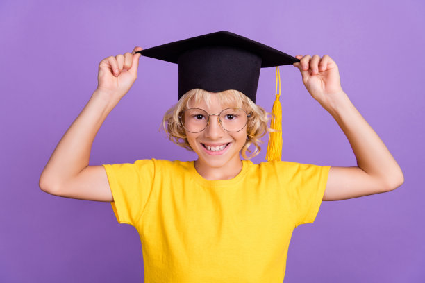 照片中相当滑稽的男生穿着黄色的t恤，戴着眼镜，双臂微笑，毕业帽，孤立的紫罗兰色背景图片下载