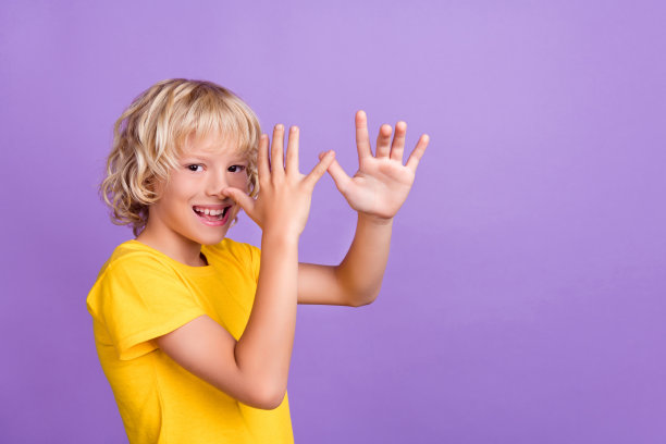 照片欢快的年轻快乐的正面男孩愚弄手的手指鼻子笑话孤立在紫色背景图片下载