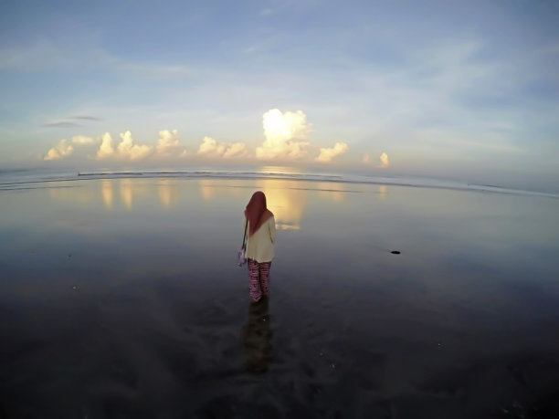 在一个阳光明媚、凉爽的早晨，你可以看到一个戴着头巾的女人笔直地站在一个美丽而干净的海滩上看着美丽的风景图片下载