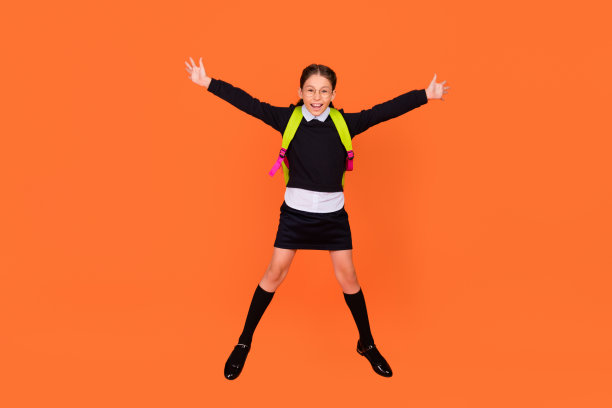 欢快快乐的女学生跳起来的全身照片，戴着背包眼镜孤立在橙色背景上图片下载