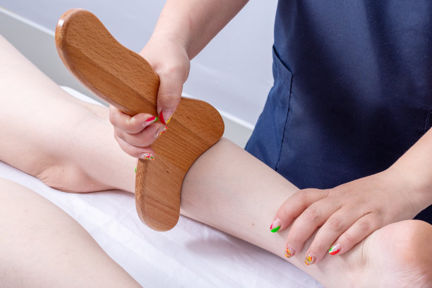 女按摩师用木制按摩器按摩女人腿的背部肌肉。身体护理的概念图片下载