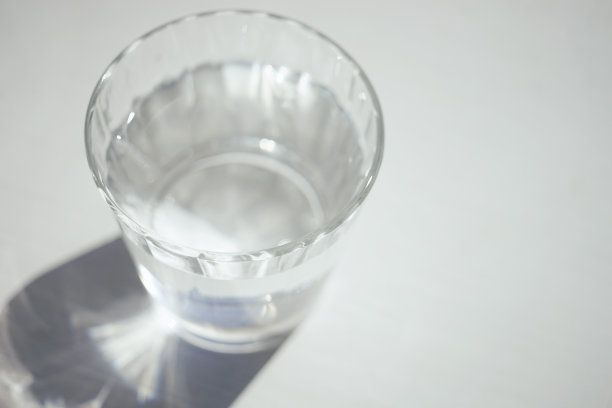 满玻璃杯的水在白色阳光下的桌子上有阴影图片下载