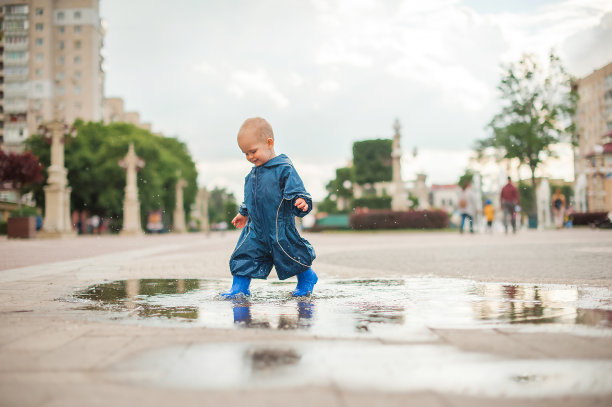 快乐的蹒跚学步的孩子穿着蓝色连体衣走过水坑，溅起的特写和复制空间…图片下载