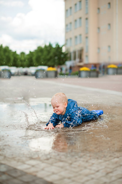 快乐的蹒跚学步的孩子穿着蓝色连体衣走过水坑，溅起的特写和复制空间…图片下载