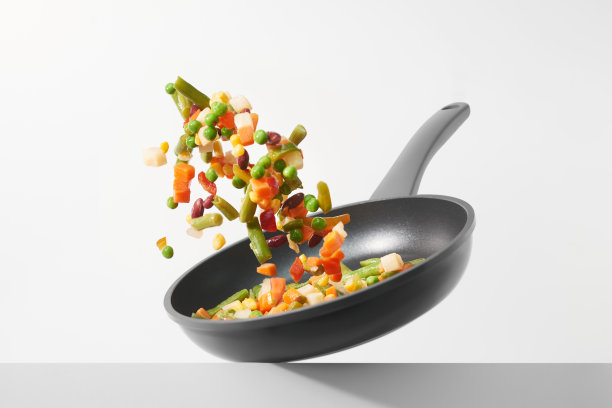 新鲜的蔬菜在白底的平底锅里飞来飞去。在平底锅里煮各种切碎的蔬菜。健康饮食的概念。“n图片下载