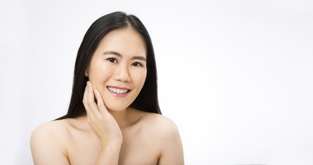 美丽的亚洲女人的肖像与完美的健康光泽的皮肤，手触摸下巴在白色的背景，年轻美丽的亚洲女孩与漂亮的微笑的脸护理。美容韩国水疗护肤。图片下载