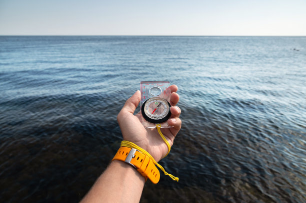 一名男子的手戴着腕带，在大海的背景下拿着一个磁罗盘图片下载