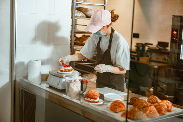 在工艺烘焙店，戴面具的糖果师将草莓片放在奶油牛角面包上图片下载