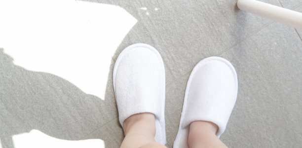 孩子穿着白色的旅馆拖鞋。用毛巾擦拭客人的一次性水疗鞋。前视图。图片下载