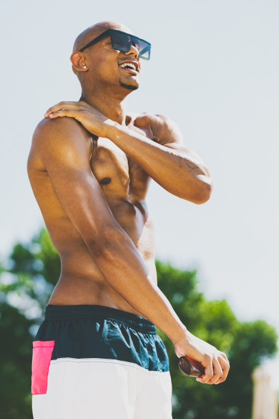 阳光明媚的夏日，一个年轻英俊、肌肉发达的男子在海滩上做日光浴。图片下载