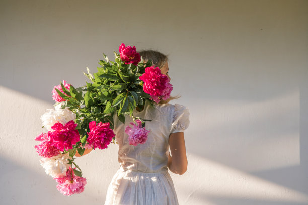 网上交友。户外的照片，年轻的红发女子穿着复古的婚纱，手里拿着一大束粉红色的牡丹。图片下载