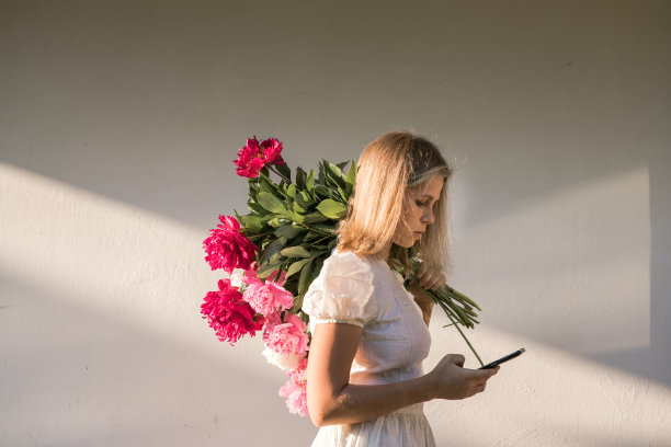 网上交友。户外的照片上，年轻的红发女子穿着复古的婚纱，手拿一大束粉红色的牡丹花图片下载