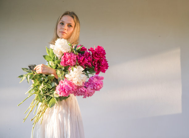 网上交友。户外的照片，年轻的红发女子穿着复古的婚纱，手里拿着一大束粉红色的牡丹。图片下载