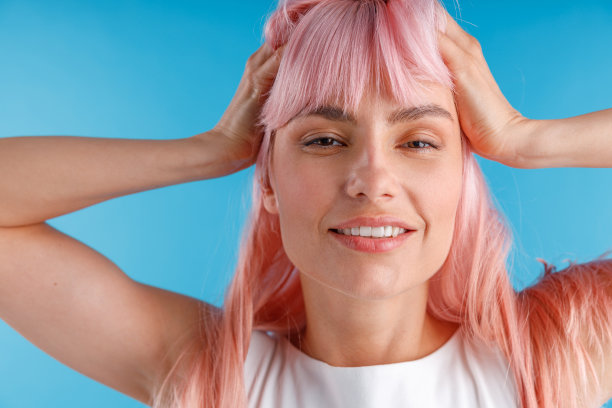 近距离的照片，美丽的女模特与粉红色的头发微笑对相机，而摆出孤立在蓝色的工作室背景图片下载