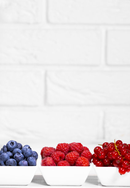 新鲜的生浆果放在白色的陶瓷碗里，白色的背景。空间的文本。红醋栗，覆盆子和蓝莓，夏季水果，垂直分辨率图片下载