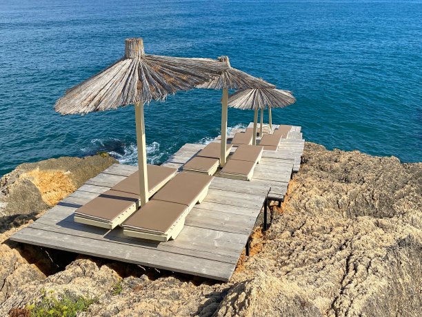 夏日美丽的海滩。稻草遮阳伞和躺椅背对着平静的蓝色海水和多云的天空。美好的夏天。在地中海海岸度过轻松的假期。图片下载