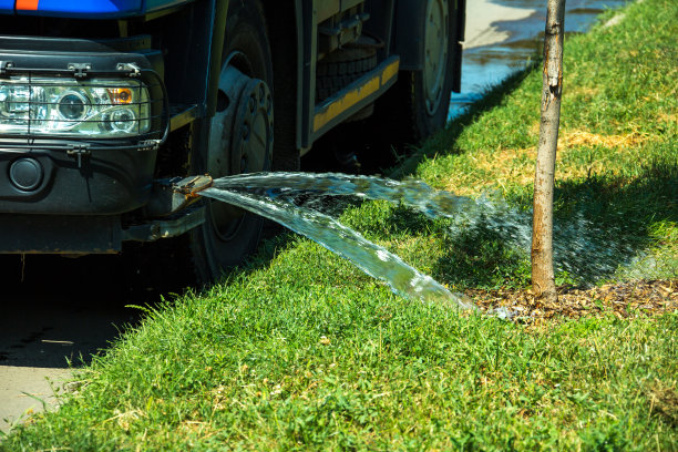 一辆给草坪浇水的卡车用喷水器把水浇在草坪上。城市草坪养护服务。图片下载