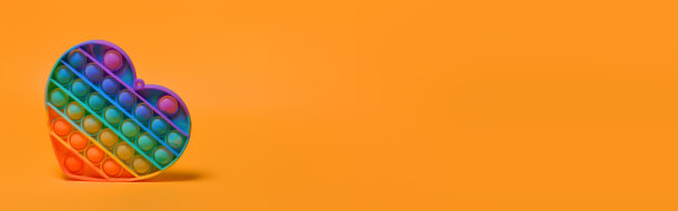 流行它-新的流行的彩色硅胶感官时尚玩具抗压力的形式在一个橙色的背景上的心。彩虹的颜色。副本的空间。横幅图片下载