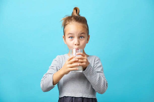 美丽的小女孩喝着牛奶，站在蓝色的孤岛上。图片下载