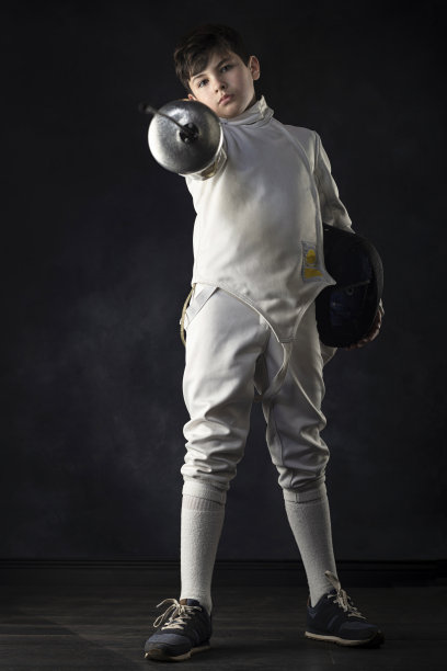 身穿击剑服的男孩在黑色背景下看着相机拍照。图片下载