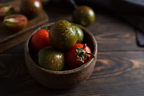 新鲜的黑番茄番茄的微距摄影。棕色木制背景上的Kumato品种。陶瓷盘子里的蔬菜。蔬菜的深色照片。番茄上的水滴。生图片下载