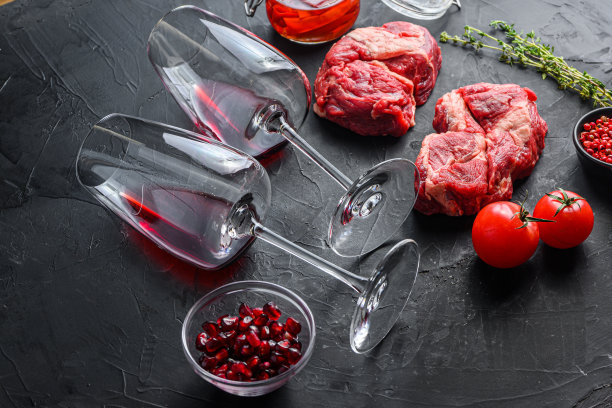 配上红酒酒杯，靠近生的有机牛排，配上迷迭香，辛辣的辣椒油在黑色纹理的背景侧面。图片下载