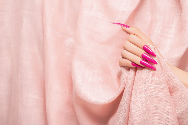 女性手与粉红色细高跟鞋指甲设计。长指甲修指甲。女人手放在浅粉色织物背景上图片下载