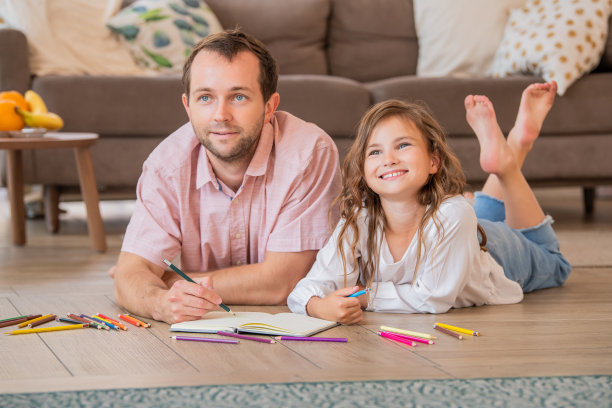父亲和女儿躺在公寓房间的地板上画画。图片下载