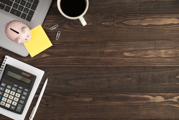 俯视图照片的小猪银行黄色贴纸笔记纸笔记本电脑，咖啡杯，白色夹子，笔和计算器在笔记本上孤立的深色木桌背景与copyspace图片下载