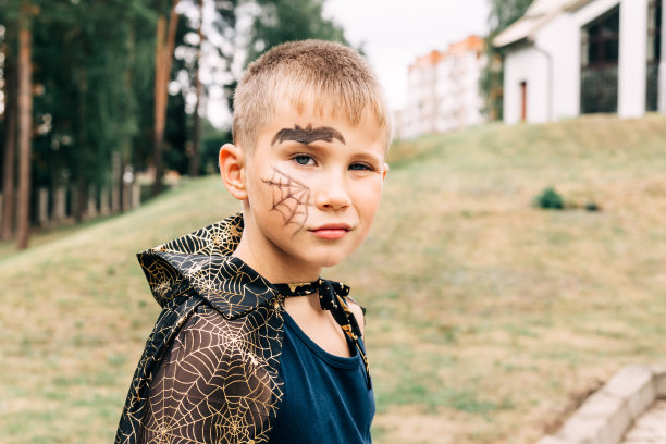 在公园里，一个男孩穿着吸血鬼万圣节服装，画着一张脸看着镜头。本空间图片下载