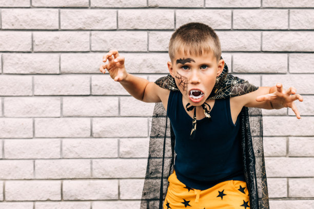 在公园的镜头前，一个男孩穿着吸血鬼万圣节服装，脸上画着尖牙。本空间图片下载