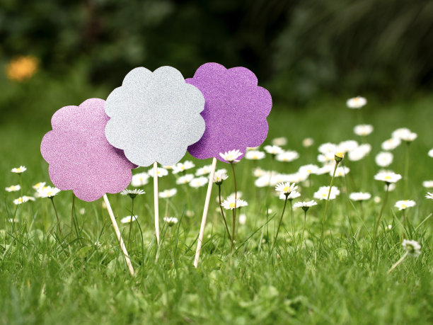 三朵闪闪发光的纸花，粉红色、银色和紫色的，和雏菊在草地上。图片下载