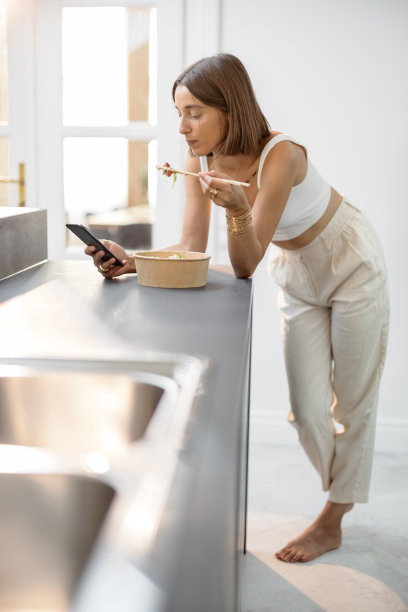 厨房里拿着亚洲外卖和智能手机的女人图片下载