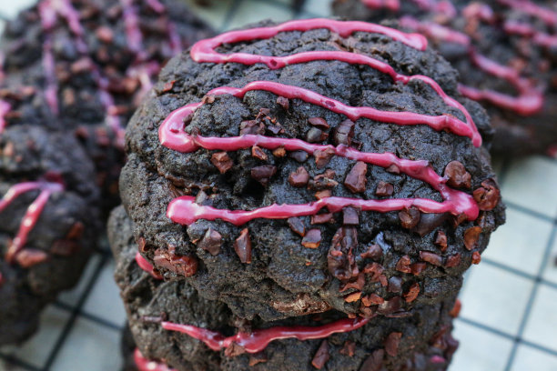 特写图片是一堆新鲜烘焙的，自制的，巧克力片黑森林饼干，装饰着粉红色的水糖霜，在电线上，金属冷却架上面的防油纸羊皮纸，聚焦前景图片下载