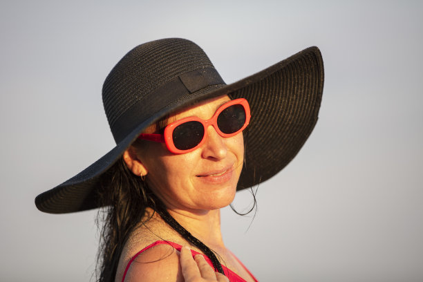 一名戴着宽边黑帽子和太阳镜的妇女看着镜头微笑着。图片下载