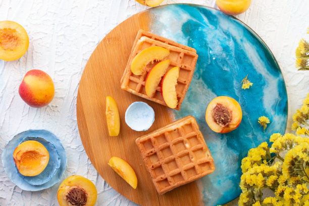 比利时自制的华夫饼，上面有桃子和黄色的花朵，还有漂亮的蓝色图案的木板。前视图。菜单的照片。早餐甜点，背景是白石。平躺图片下载