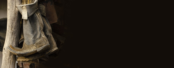 破旧的乡村靴子挂在屋顶下的柱子上。复古的鞋子。农村。深色背景，有复制空间。个人故事的概念图片下载