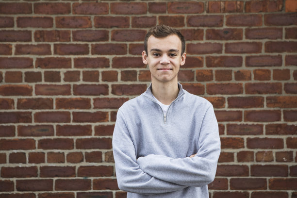 英国北部一名男大学生的肖像，他双臂交叉，站在一堵红砖墙旁图片下载