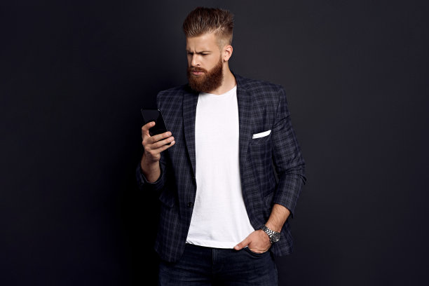 接收朋友的信息。英俊的年轻人用智能手机，站在黑色背景下微笑图片下载