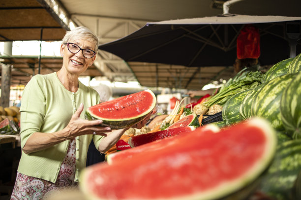 老年妇女的肖像在市场购买新鲜的有机西瓜健康营养。图片下载