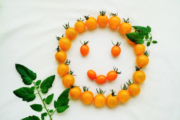 一个由许多黄色的小西红柿和它们的叶子组成的微笑在浅绿色的布背景上图片下载