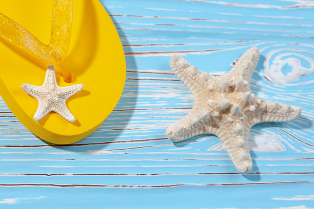 黄色橡胶沙滩人字拖和海星在蓝色木制背景下，放置文字图片下载
