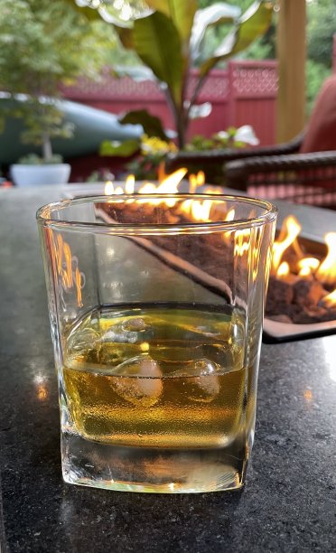一杯加冰的威士忌，在后院里有燃气壁炉图片下载