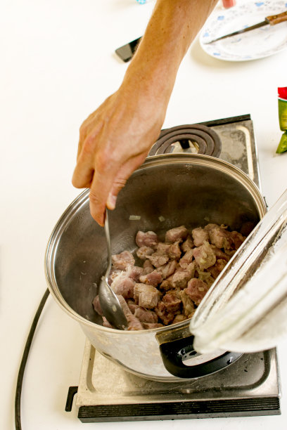 一位妇女用手在平底锅里用勺子搅拌着炸洋葱和生肉。用洋葱煮肉的过程。图片下载