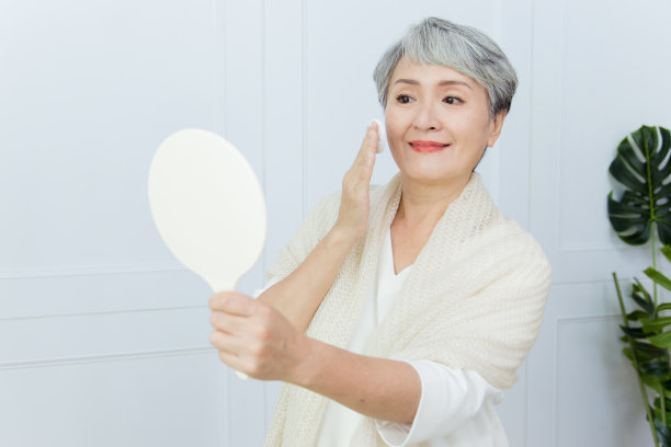 一位亚洲老妇人正拿着镜子用粉扑给自己化妆。图片下载